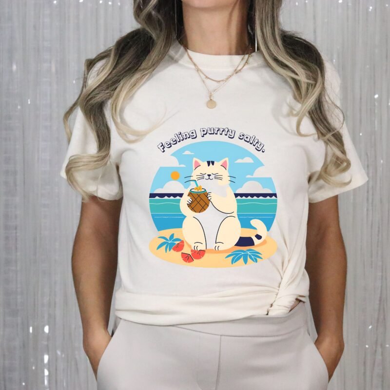 Natural beige color T-shirt with the phrase ‘Feeling purrty salty’ printed above a cat drinking pina-colada on the beach relaxing illustration