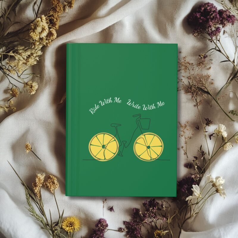 Green hardcover journal with a minimalist bicycle illustration featuring lemon slice wheels and the phrase ‘Ride With Me Write With Me’ above it.