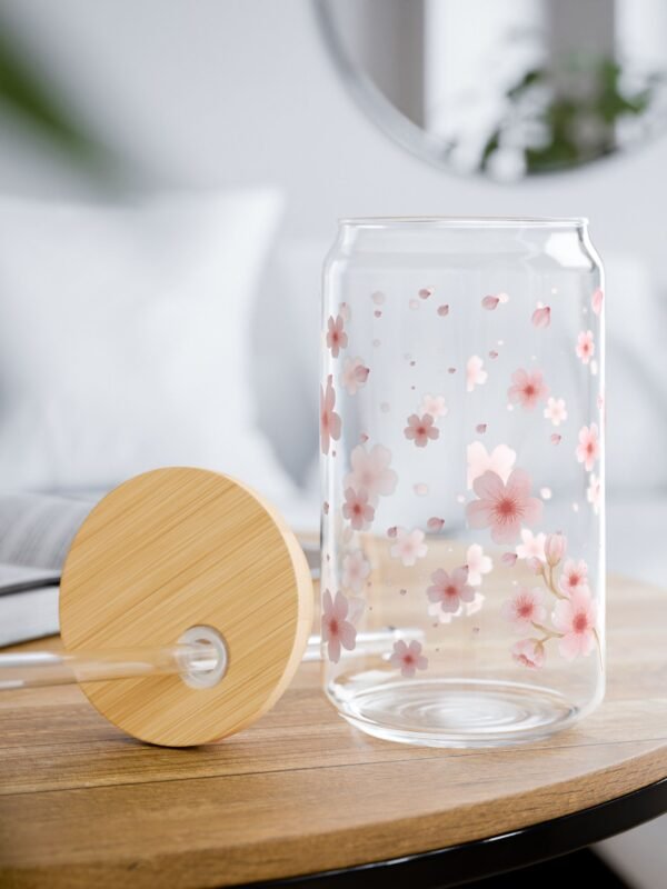 Clear glass can tumbler with pink cherry blossom design, bamboo lid, and glass straw on wooden table