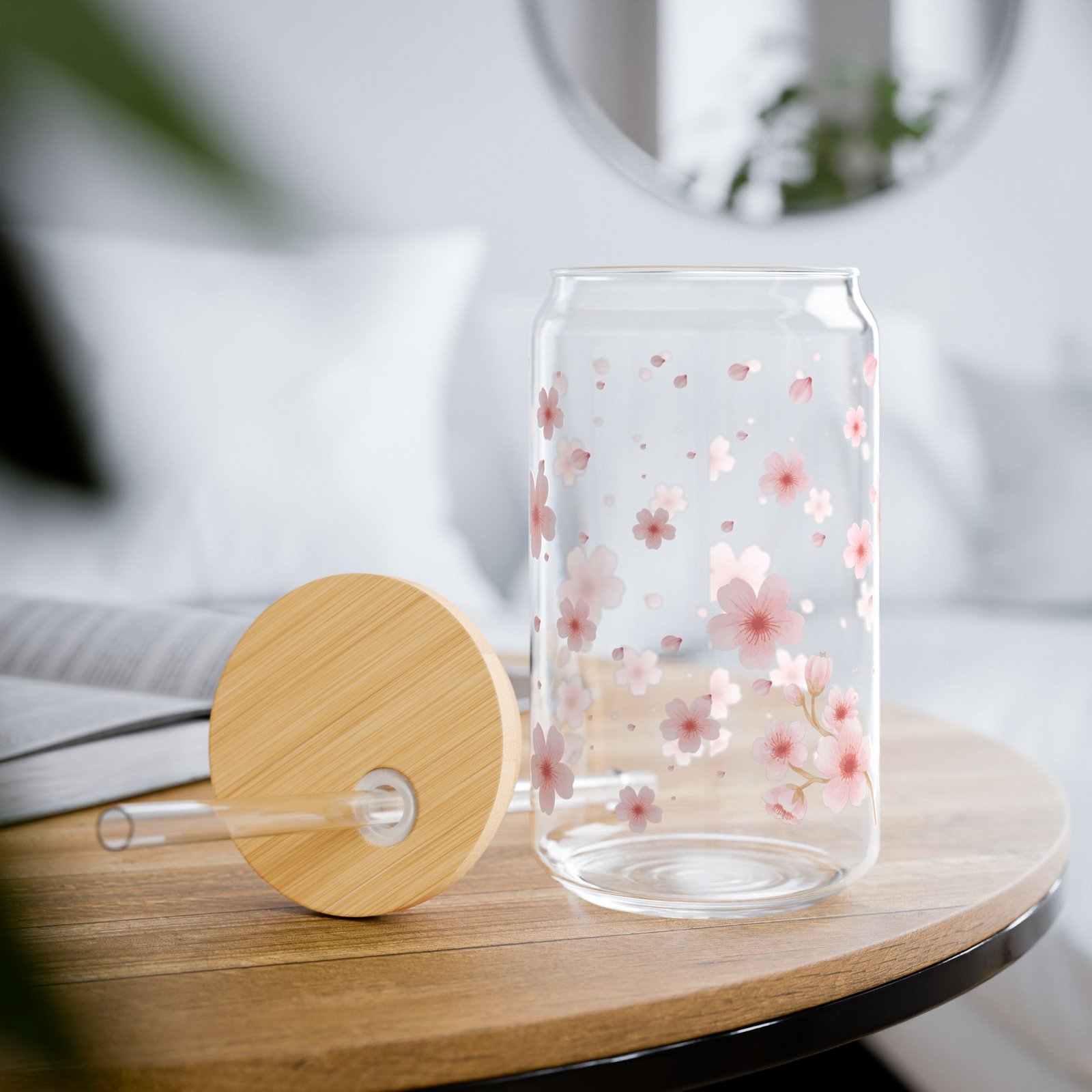 Clear glass can tumbler with pink cherry blossom design, bamboo lid, and glass straw on wooden table