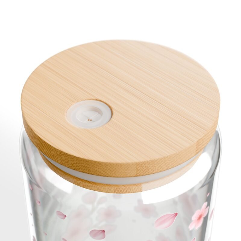 Clear glass can tumbler with pink cherry blossom design, bamboo lid, and glass straw on wooden table