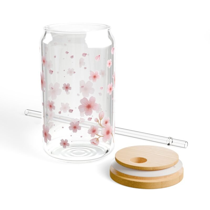 Clear glass can tumbler with pink cherry blossom design, bamboo lid, and glass straw on wooden table