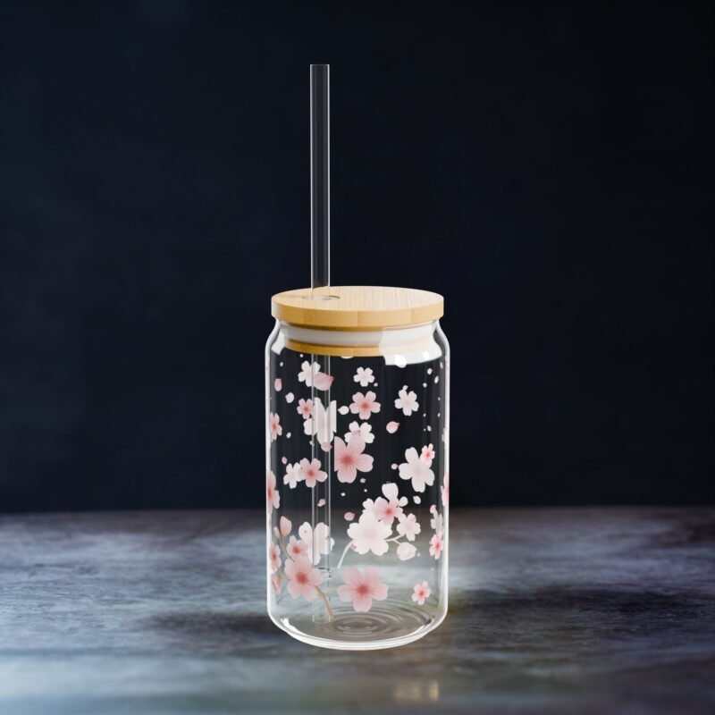 Clear glass can tumbler with pink cherry blossom design, bamboo lid, and glass straw on wooden table
