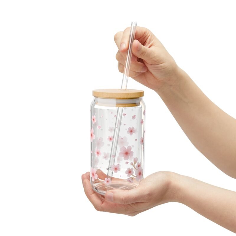Clear glass can tumbler with pink cherry blossom design, bamboo lid, and glass straw on wooden table