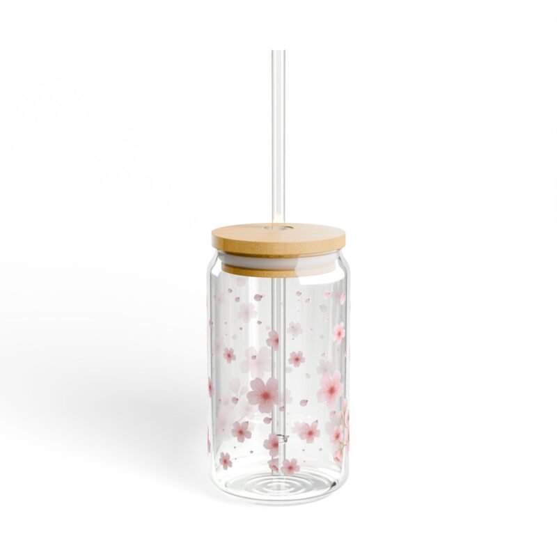 Clear glass can tumbler with pink cherry blossom design, bamboo lid, and glass straw on wooden table
