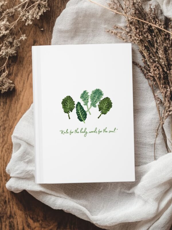 White Matte hardcover journal with the phrase ‘KALE for the body, words for the soul" printed below illustrations of leafy greens kale, placed on a white cloth with dried flowers.