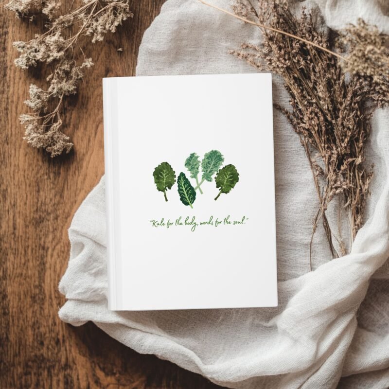 White Matte hardcover journal with the phrase ‘KALE for the body, words for the soul" printed below illustrations of leafy greens kale, placed on a white cloth with dried flowers.